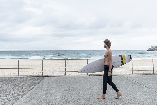 Man carrying surfboard along promenade, Bondi Beach