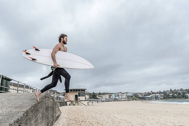 istock Man leaping off wall with surfboard, Bondi Beach 503888928