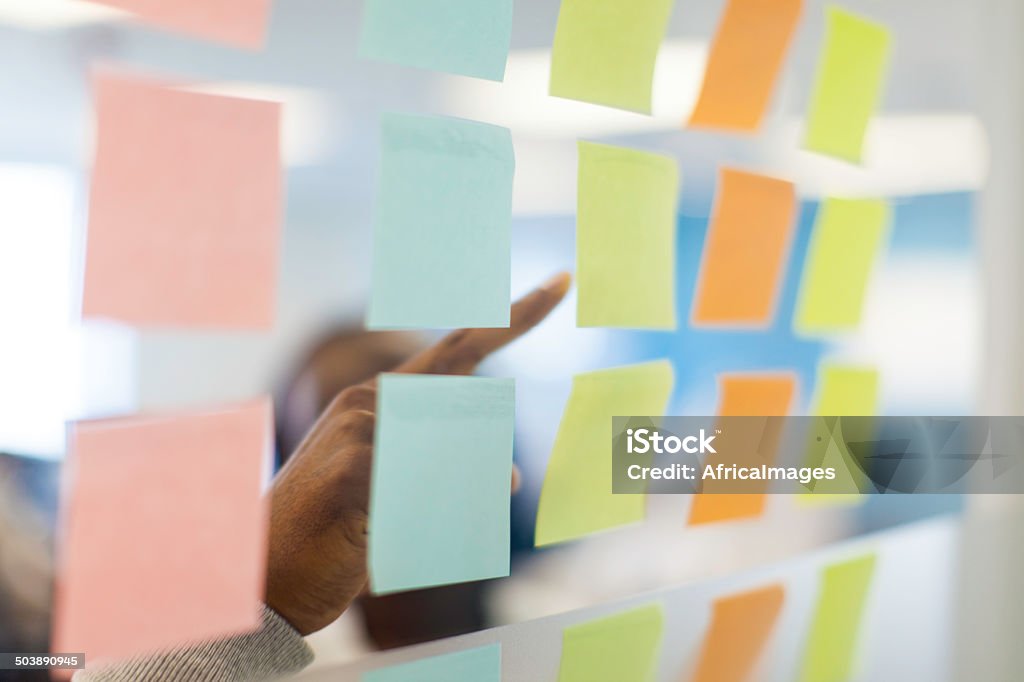 Close up of a businessman pointing at a sticky note. Close up of an african businessman pointing at a sticky note. Cape Town, Western Cape, South Africa Accuracy Stock Photo