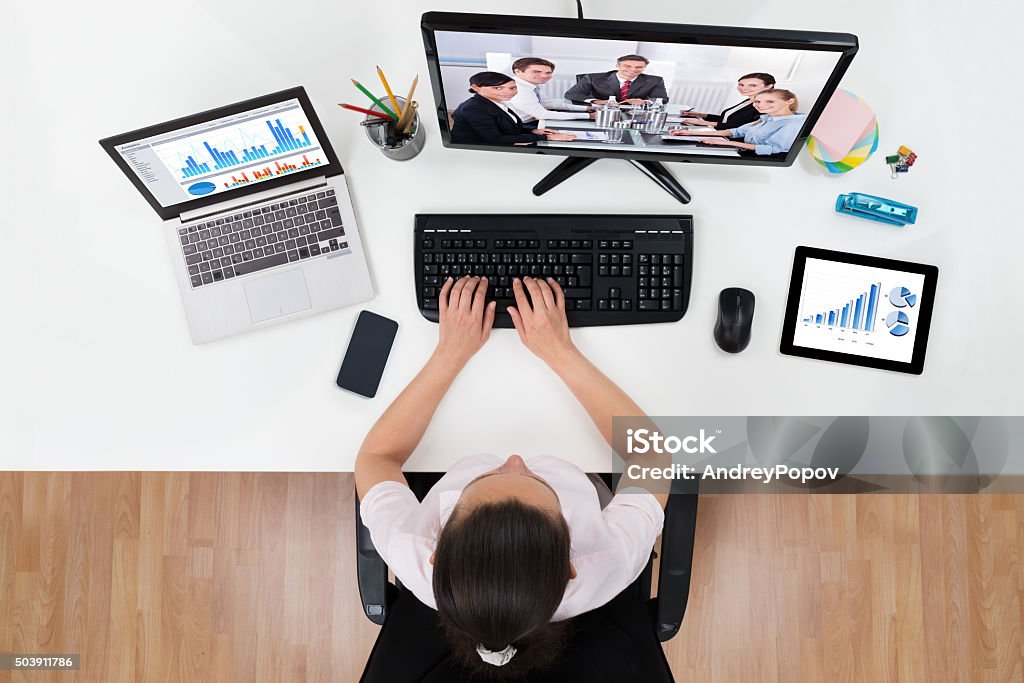 Businesswoman Videoconferencing With Co-workers On Computers Young Businesswoman Videoconferencing With Co-workers On Computers At Desk Web Conference Stock Photo