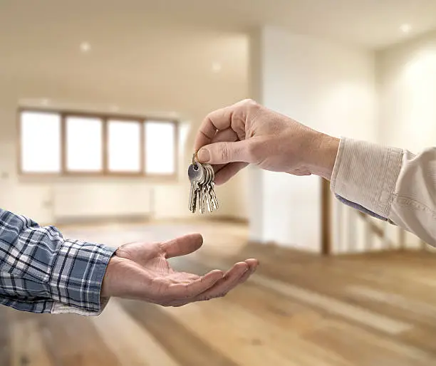 Real Estate Agent giving house key to buyer in empty room