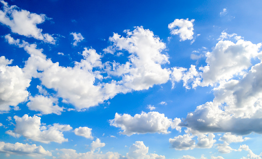 Panoramic view of a bright blue sky filled with fluffy white clouds. The clouds vary in size and are spread across the sky, suggesting a vast open atmosphere. The blue of the sky is a clear, vibrant hue that suggests a sunny day. There is a serene and tranquil quality to the scene, which may evoke feelings of calmness and openness.