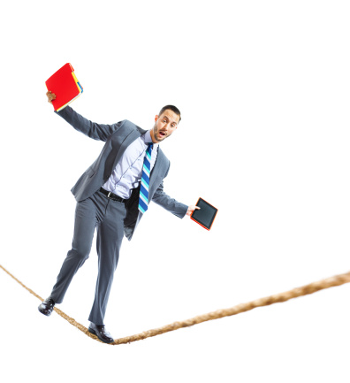 A young businessman holding mobile phone and tablet computer walking the tightrope balancing himself.