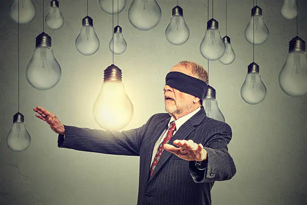 Blindfolded senior elderly man walking through light bulbs searching for bright idea