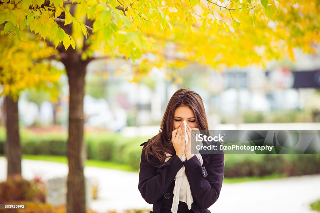 Allergy season Young girl in autumn park blowing nose. Standing in park in warm clothing. Allergy Stock Photo