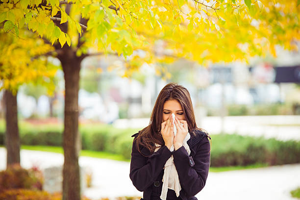 Allergy season Young girl in autumn park blowing nose. Standing in park in warm clothing. cold virus stock pictures, royalty-free photos & images