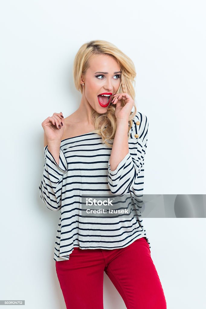 Excited blonde woman wearing striped blouse and red trausers Portrait of excited beautiful blonde woman wearing striped blouse and red trausers, laughing. Adult Stock Photo