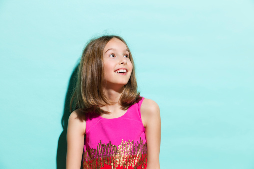 Surprised and happy girl looking away. Waist up studio shot on teal background.