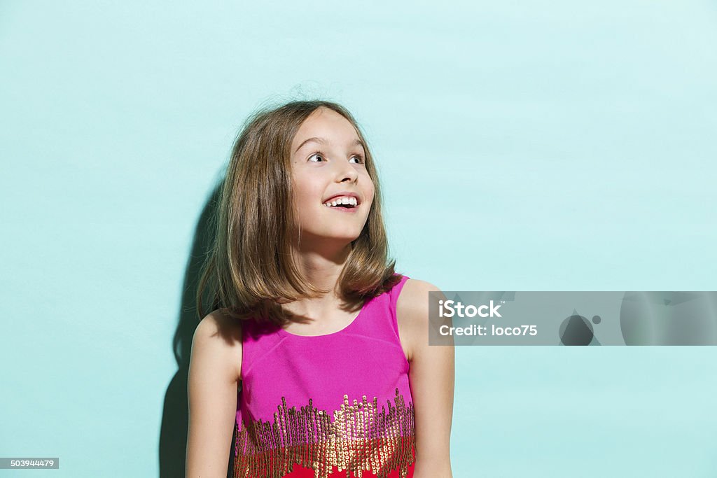 Smiling girl on turquoise background looking up Surprised and happy girl looking away. Waist up studio shot on teal background. Girls Stock Photo