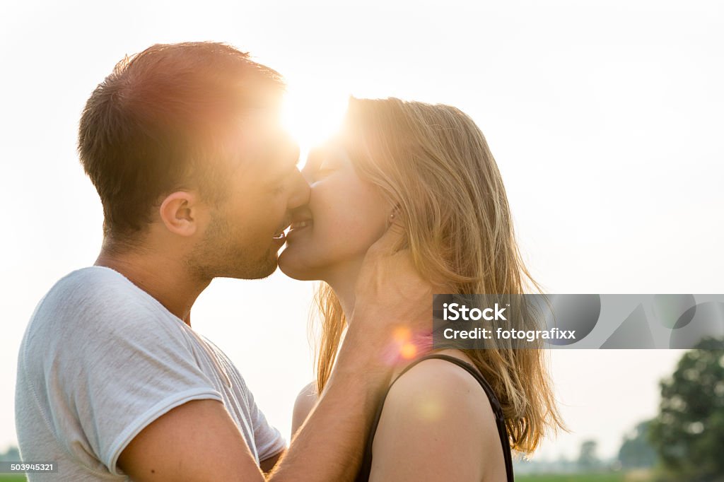 summer portrait of a kissing young adult couple, back lit young couple in love, Kissing Stock Photo