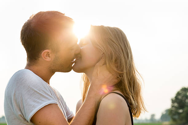 summer portrait of a kissing young adult couple, back lit stock photo