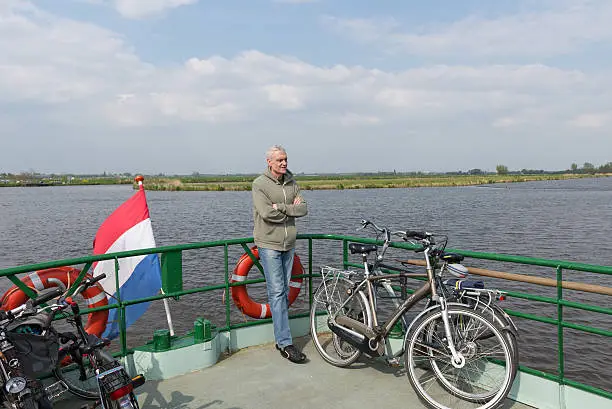 Man stands on ferryboat with bicycles, Dutch flag and life buoys