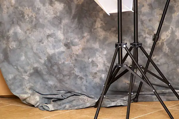 View behind the scenes of mottled background and light stand tripod legs at photo studio.
