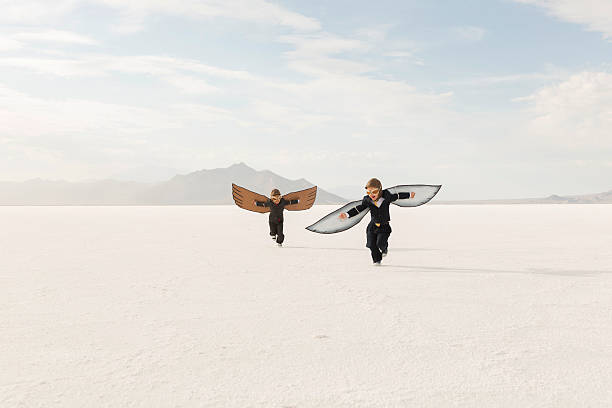 Two young business boys dressed in business suits wearing cardboard wings and aviator goggles are ready to fly their business into the sky. The boys are running on the Bonneville Salt Flats in Utah, USA.