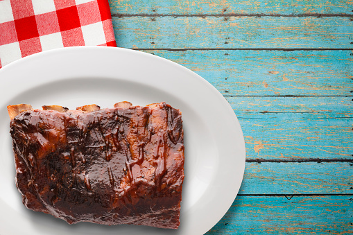 Traditional slow smoked thick cut BBQ pork ribs sauced, plated on napkin and blue rustic background
