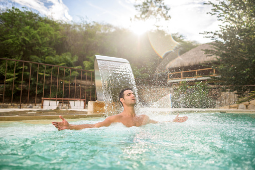 Handsome Latin American man at the spa enjoying the hydrotherapy in the swimming pool and relaxing