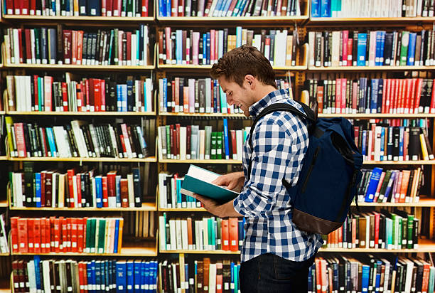 istock Male student reading book in library 503989968