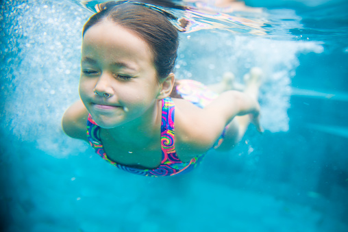 Close up of young girl swimming underwater in a swimming pool. Little girl is holding her breath and have her eyes closed. She looks confident, determined.