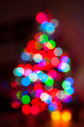 Illuminated New year tree shaped  blurred bokeh light background. Multicolored vibrant vertical image.