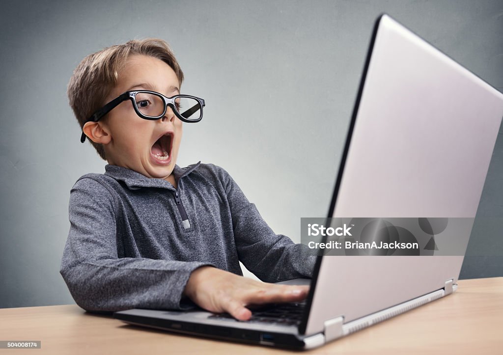 Shocked and surprised boy on the internet with laptop computer Shocked and surprised boy on the internet with laptop computer concept for amazement, astonishment, making a mistake, stunned and speechless or seeing something he shouldn't see Child Stock Photo