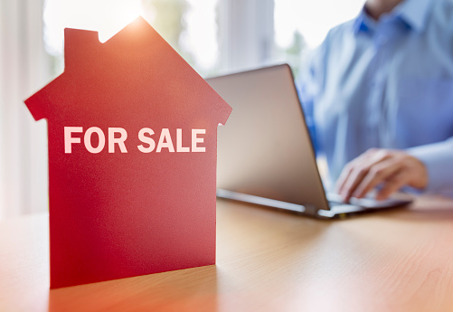 Man using laptop searching for real estate or new house on the internet with for sale sign on red house