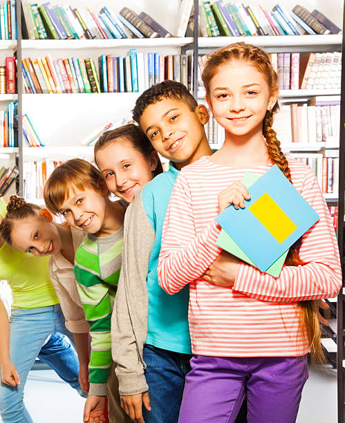 Five funny children playing and standing in a row in accordance with their height in a library