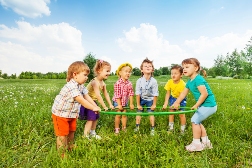 Smiling children holding one hoop together standing on green grass