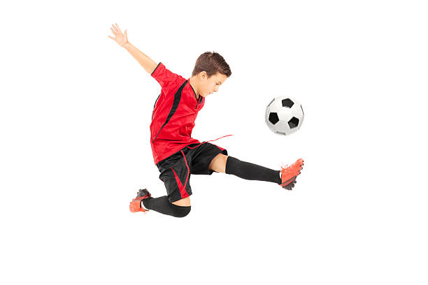 Boy, child, football player in uniform training, kicking ball with knee in mid-air in motion against white studio background. Concept of professional sport, championship, youth league, hobby. Ad