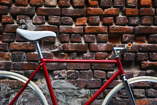 Detail of a red fixie bike, in front of a red brick wall.