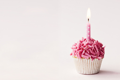 Cupcake decorated with pink chocolate curls and a single candle