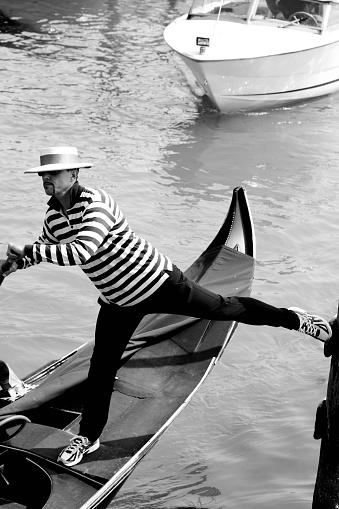 Venice, Italy - April 11, 2015: Gondola on Venice Lagoon with the gondolier doing an acrobatic push off from a mooring pole. There is a vaporetto approaching from the top of the frame.
