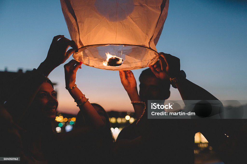 Friends releasing paper lantern in the sky at night Group of  friends on the rooftop releasing chinese lantern Lantern Stock Photo