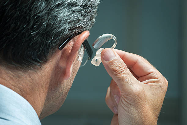 Hearing Aid Man inserts hearing aid in his ear hearing loss photos stock pictures, royalty-free photos & images