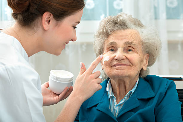 Elderly woman is assisted by nurse at home Nurse assists an elderly woman with skin care and hygiene measures at home personal care aid stock pictures, royalty-free photos & images