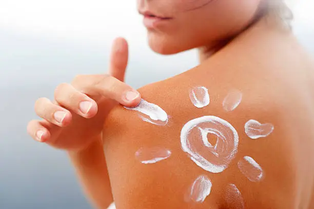 Dark tanned body of young woman in summer with sunscreen  lotion in shape of sun