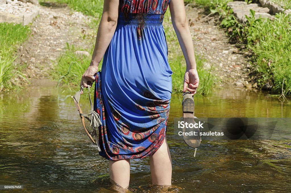 girl holds sandals wade barefoot flowing stream girl holds gray summer sandals and wade barefoot through the fast flowing stream in the park track Adult Stock Photo