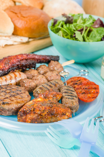 Assorted barbequed meat and bread on a blue background. Served with coleslaw, yoghurt and cucumber dip and chili sauce. Outdoors summer meal!