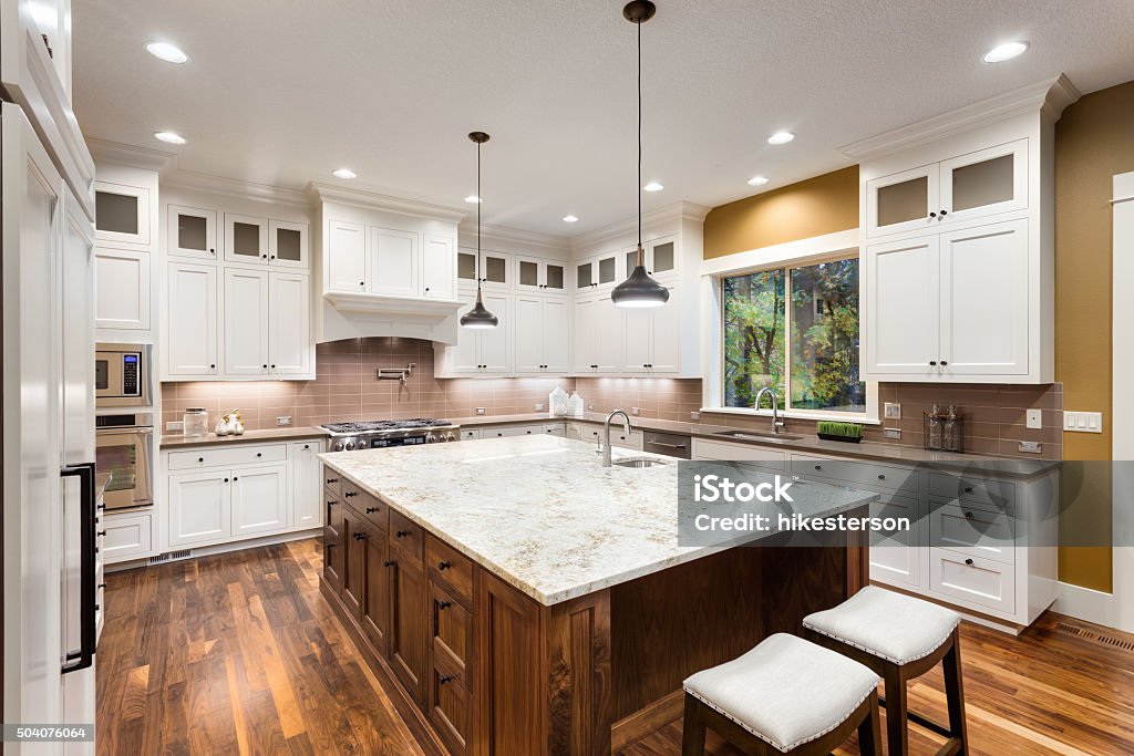 Beautiful Kitchen in Luxury Home Large Kitchen Interior with Island, Sink, White Cabinets, Pendant Lights, and Hardwood Floors in New Luxury Home Kitchen Counter Stock Photo