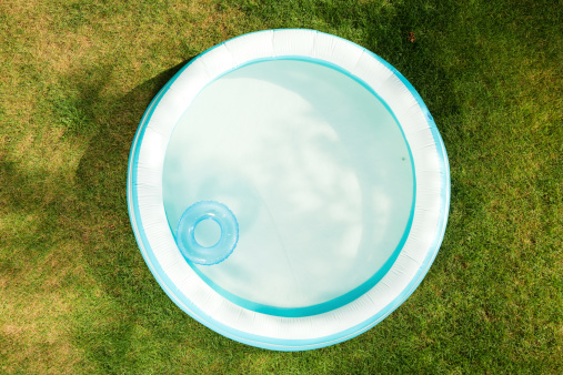 An inflatable swimming pool, partially filled with water, shot from above on dry Summer grass.