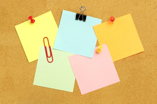 Sticky notes of various colors and fasteners clustered on a bulletin board