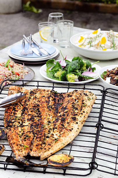 Table full of side dishes, variety assortment of salads with a whole grilled fish for a party gathering in the garden entertaining outdoors