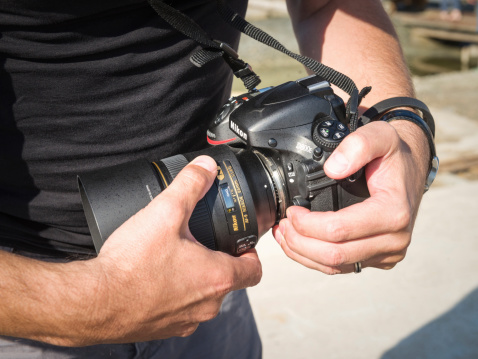 Portoroz, Slovenia - July 5, 2014: A photographer changing the lens on a Nikon D800e digital SLR camera body, holding the lens release button as he removes a Nikkor 85mm lens.