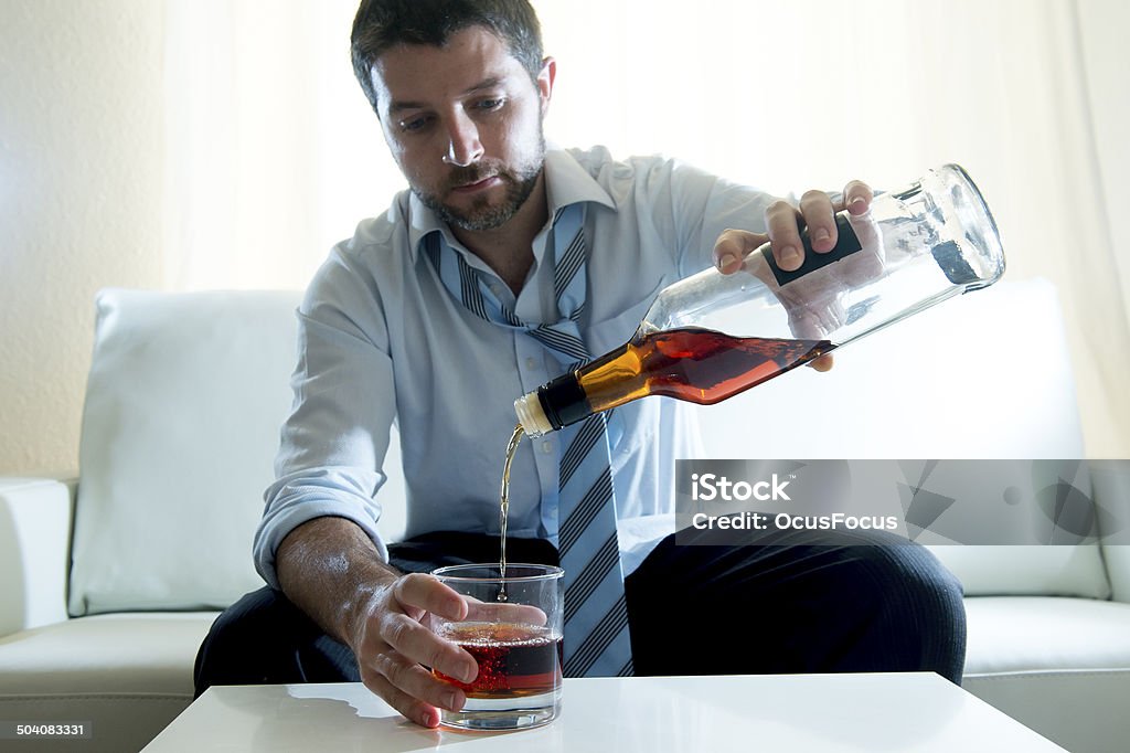 Businessman wearing blue shirt drunk at desk on white background caucasian businessman alcoholic wearing a blue work shirt and tie drunk and drinking  Scotch or Whisky sitting on a sofa at home after a long day or week of work on a white background. Abuse Stock Photo