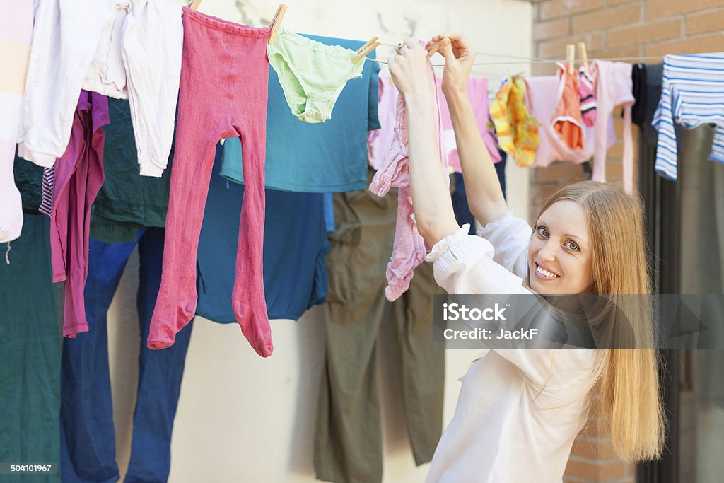 Positive long-haired girl drying clothes on clothes-line Positive long-haired girl drying clothes on clothes-line after laundry Adult Stock Photo