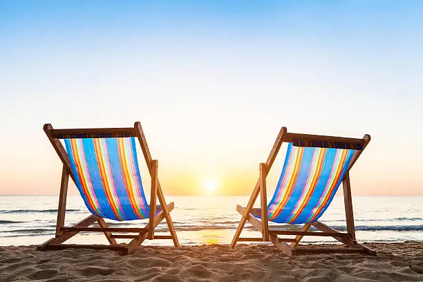 Photo of Two deck chairs on a sandy beach at sunset