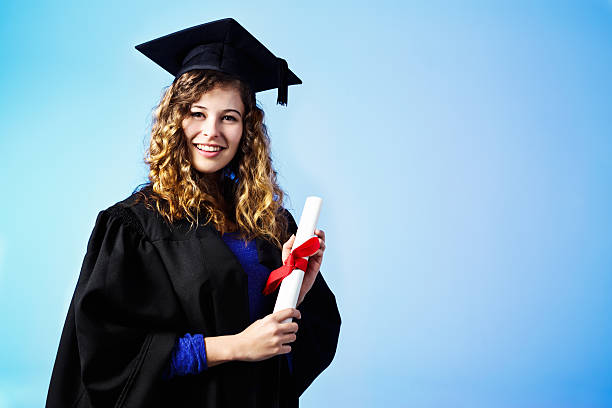 istock Pretty graduate in cap and gown holds her diploma, smiling 504105663
