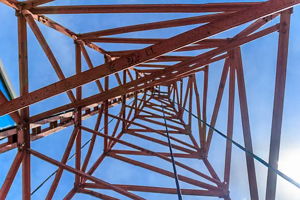 Inside derrick. pylon looking directly up at the clear blue sky. It is as if the pylon forms a metal spider's web. A tiny aeroplane seems to be caught in the bottom left corner.