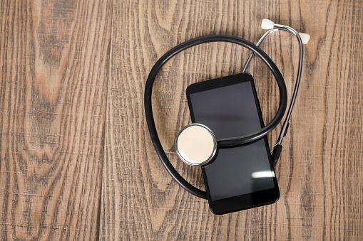 Modern smartphone with a stethoscope on a wooden background (repairing or virus protection concept).