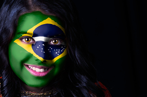 Close up portrait shot of a girl having Brazilian flag painted on her face.