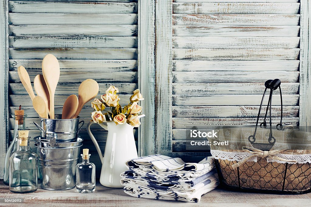 Rustic kitchen still life Rustic kitchen still life: wire basket, galvanized buckets with wooden spoons, jug with roses bunch, towels stack and glass bottles against vintage wooden shutters. Filtered toned image. Home Decor Stock Photo